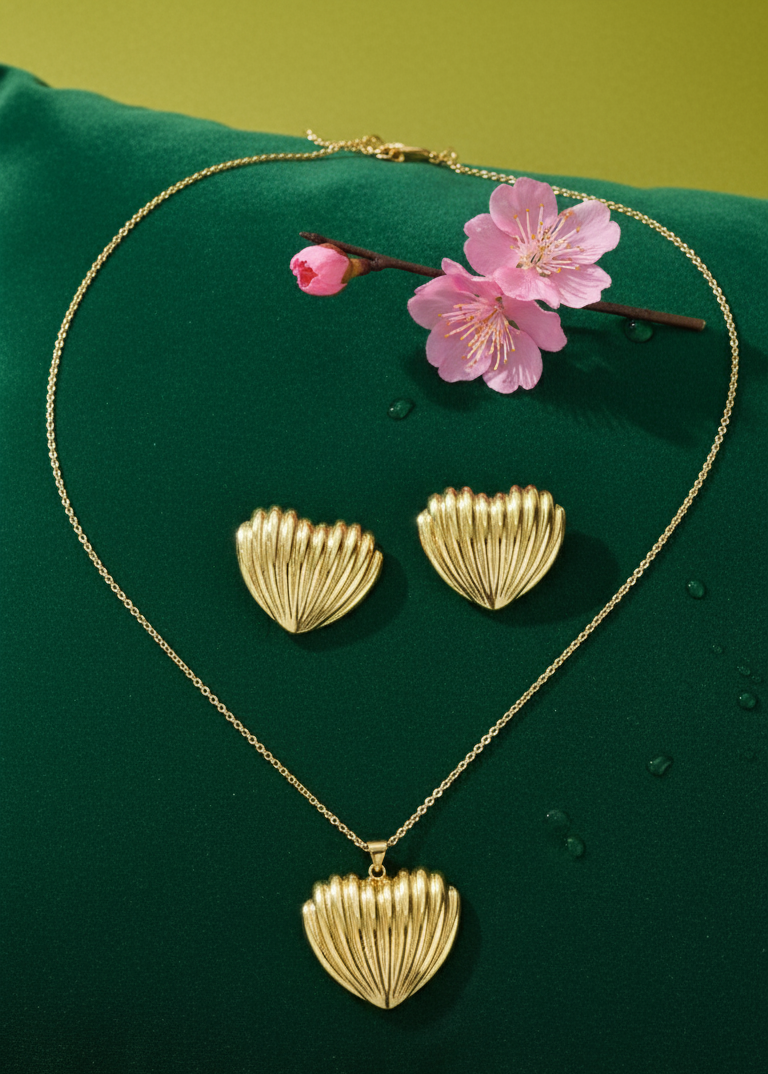 Gold heart-shaped necklace and earrings on a green background with pink flowers.