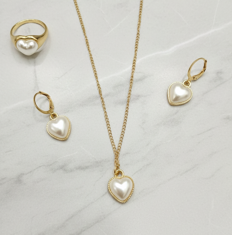 Jewelry set with heart-shaped pearl pendant necklace, earrings, and ring on a marble surface.