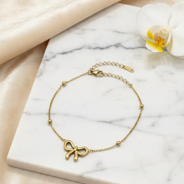 Gold bracelet with a bow charm on a marble surface