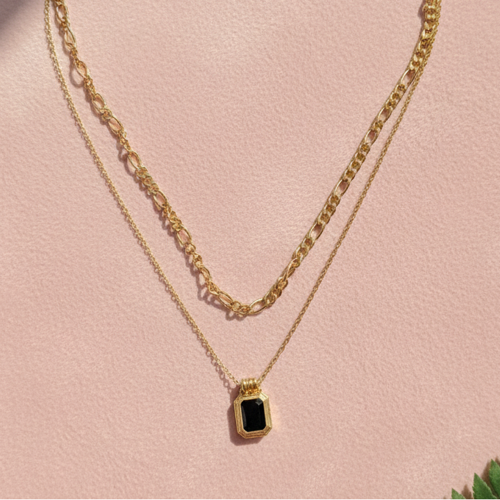 Gold necklace with a green gemstone pendant on a pink surface with a leaf