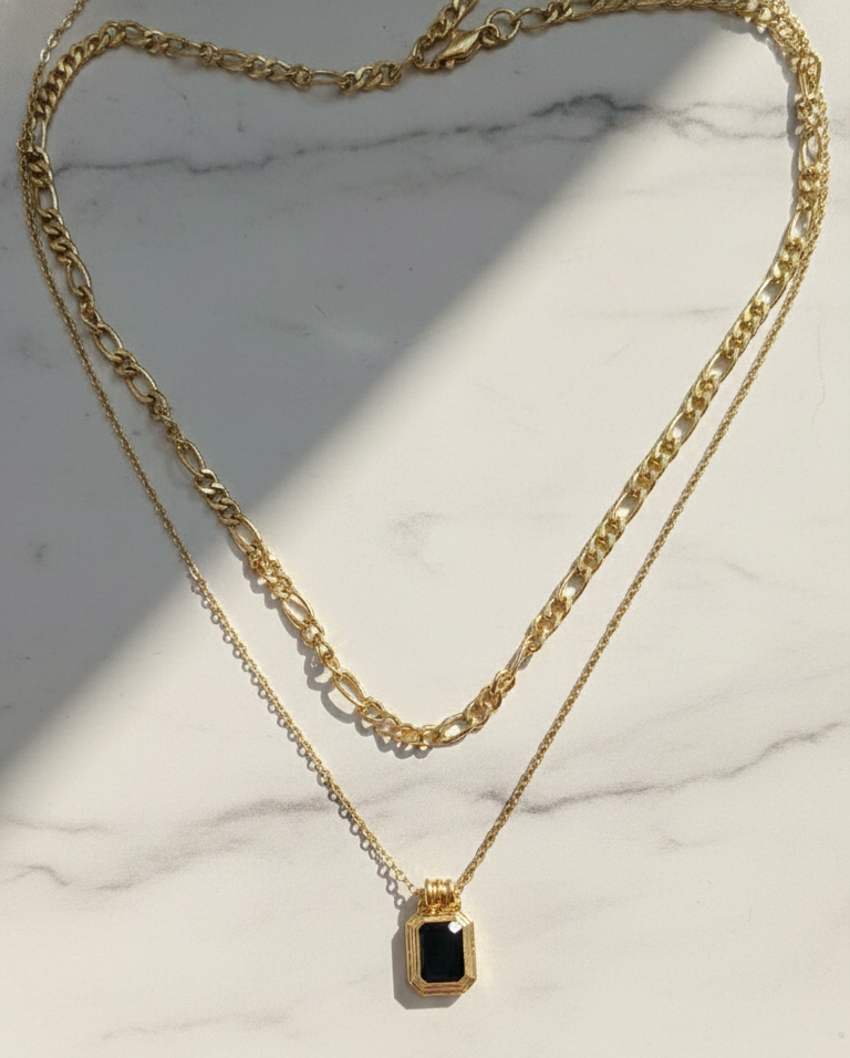 Gold necklace with a black pendant on a marble surface