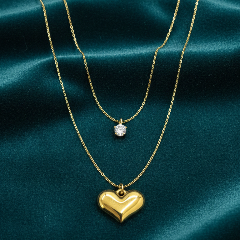 Two gold necklaces with heart pendants on a teal satin background