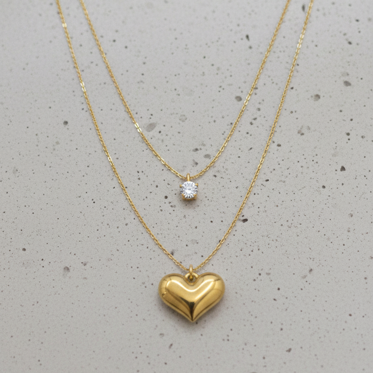 Two gold necklaces with heart pendants on a gray surface