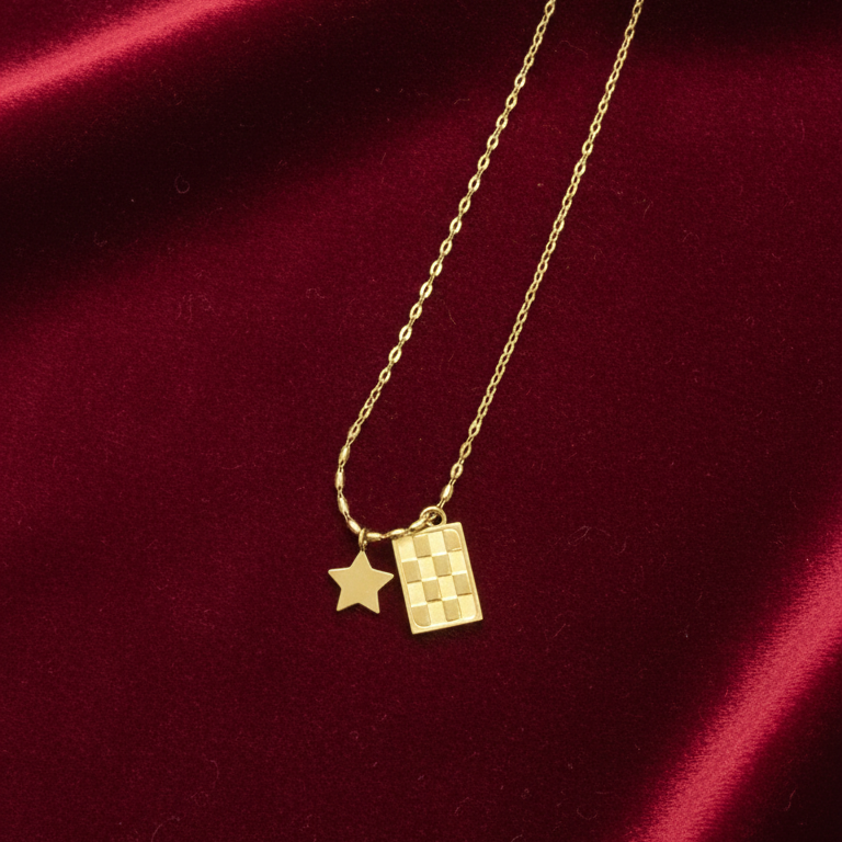 Gold necklace with star and rectangular pendant on a red satin background
